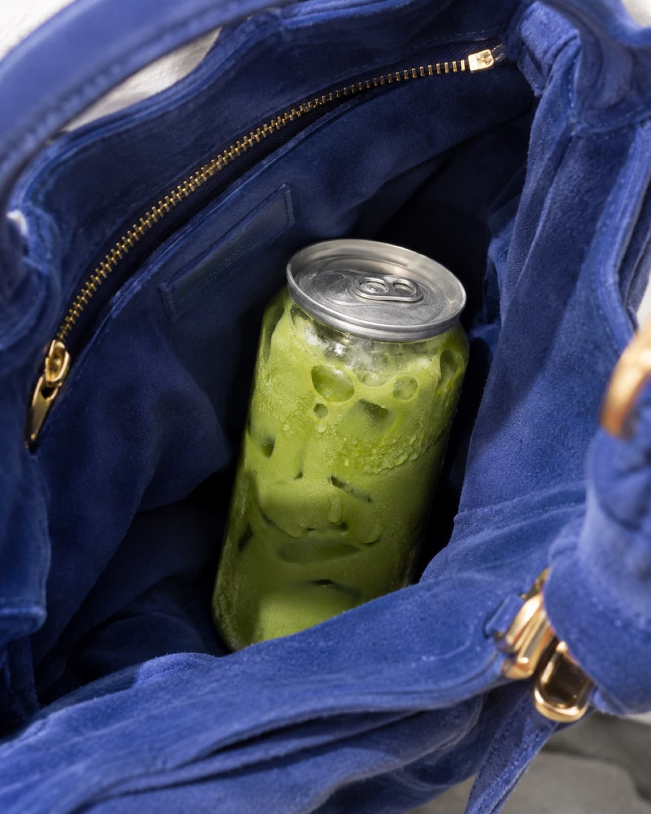 A clear can of iced matcha tucked inside a blue suede bag