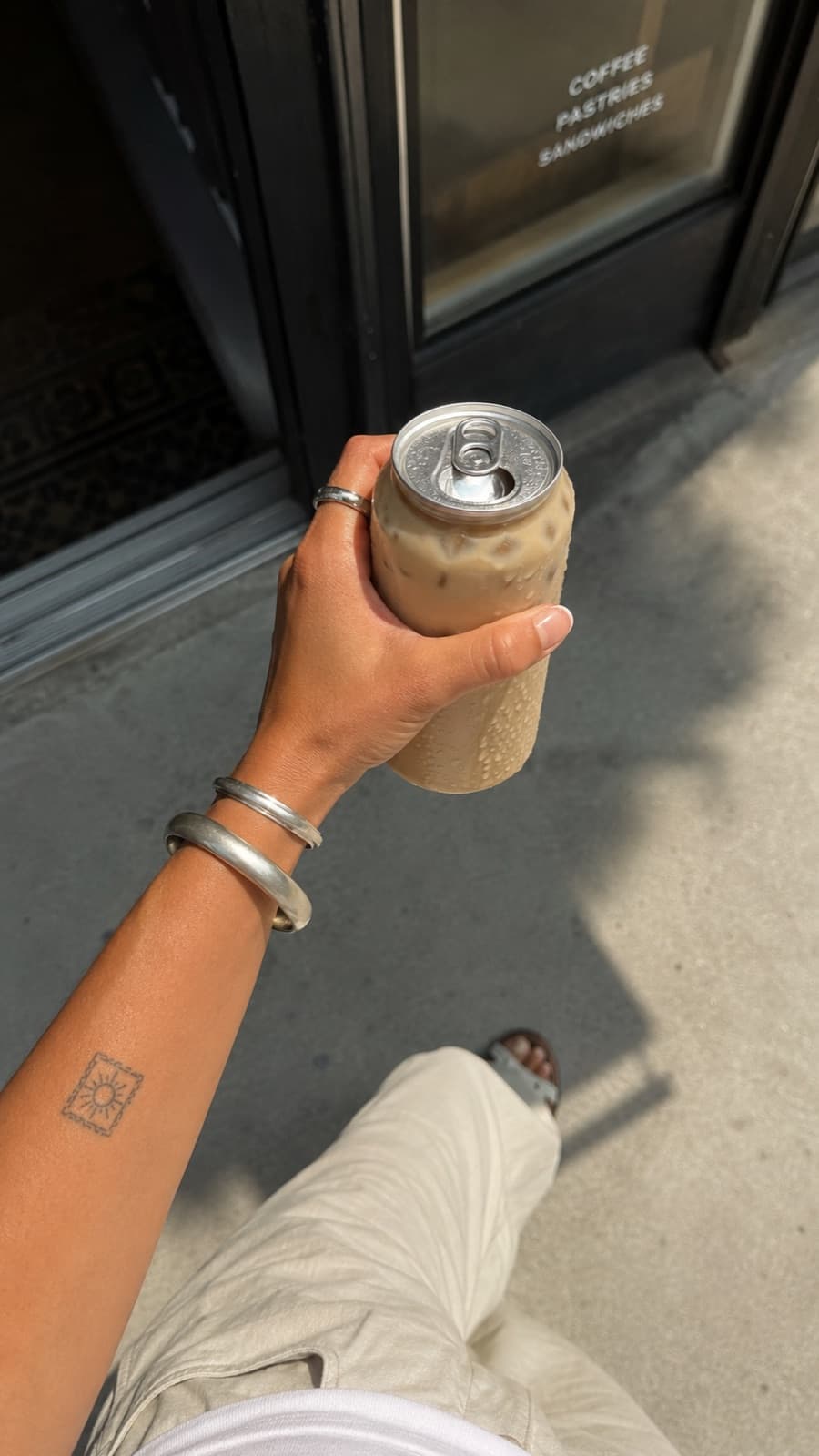 A customer holding a clear canned latte outside the coffee shop