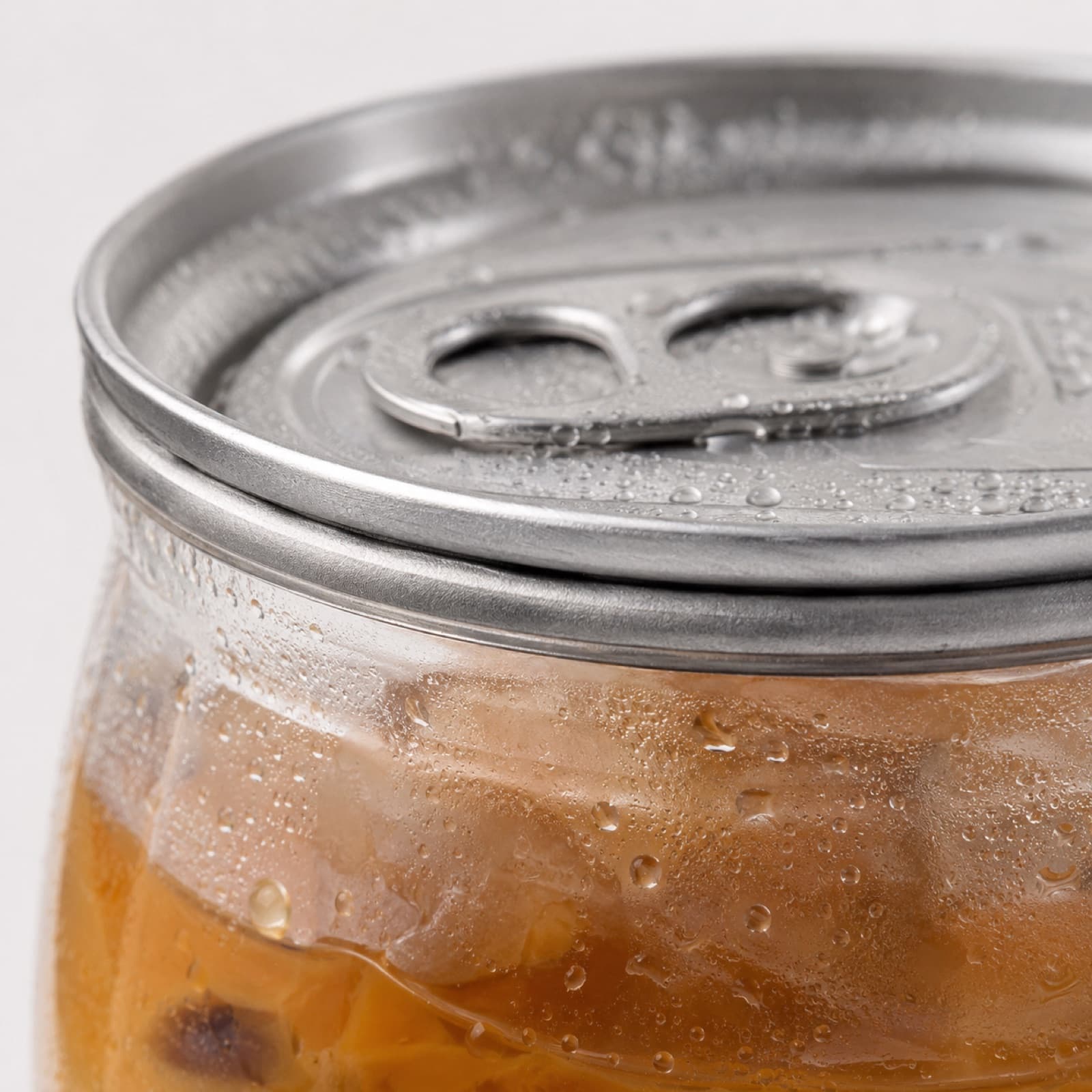 Macro shot of a freshly seamed aluminum lid on a clear can of iced coffee, beaded with condensation