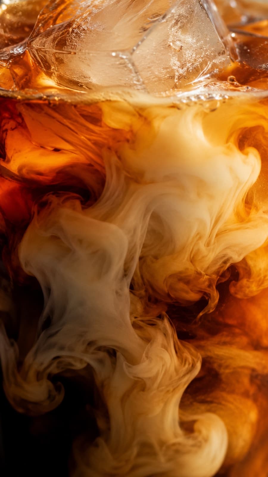 Cream swirling into iced cold brew, macro shot